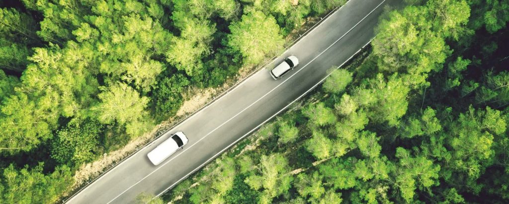 Aerial drone shot of vehicles travelling along a road with a dense forest either side